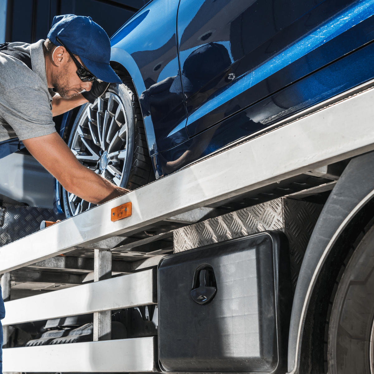 Image of an auto technician checking a blue car on a truck bed. Concept image of auto repair and maintenance at Quality Car Care in North Liberty, IA.