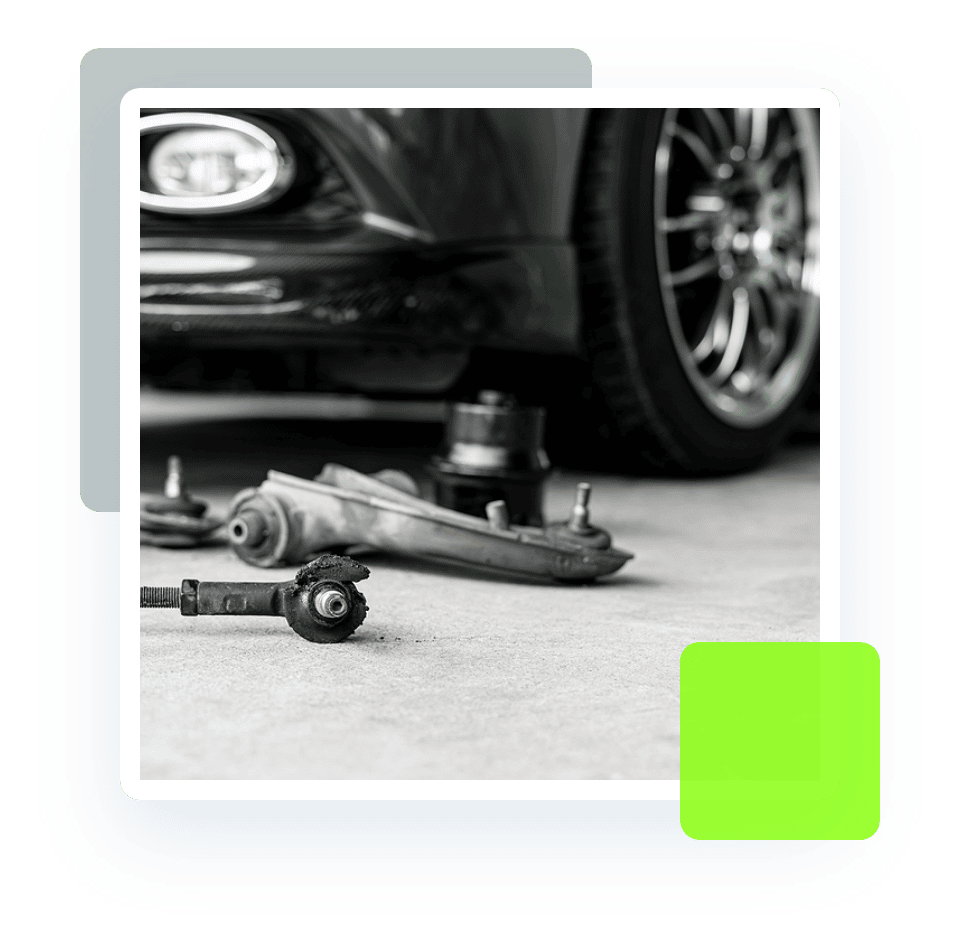 Image of a disassembled suspension parts, with a car in the background. Concept image of steering and suspension services at Quality Car Care in North Liberty, IA.