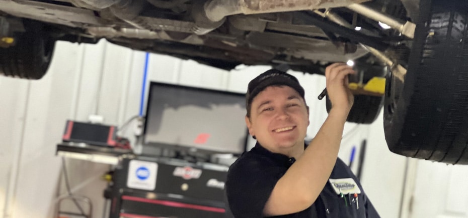 Looking for a Reliable Auto Mechanic in North Liberty, IA? | Quality Car Care. Image of Quality Car Care's mechanic, smiling while working under a lifted car.