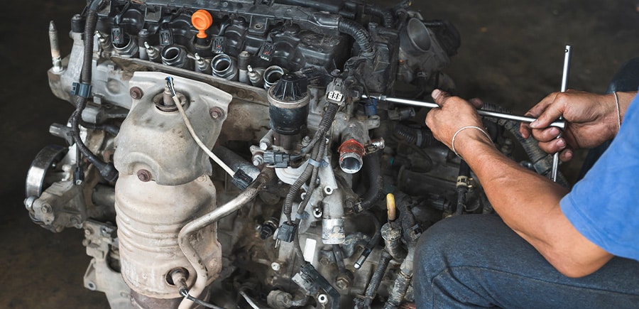 Engine Repair vs. Rebuild vs. Replacement | Quality Car Care in North Liberty, IA. Image of an engine technician working on a disassembled engine.